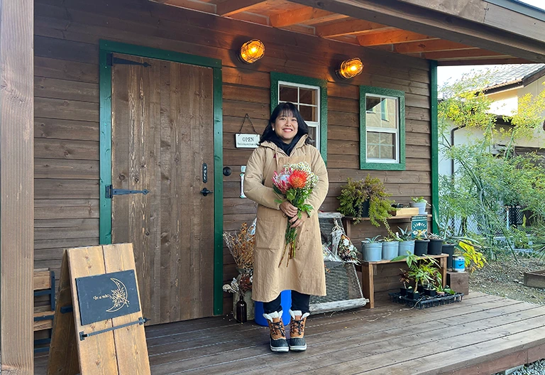 小屋店舗の前で花を持つ、お花屋さんのオーナー