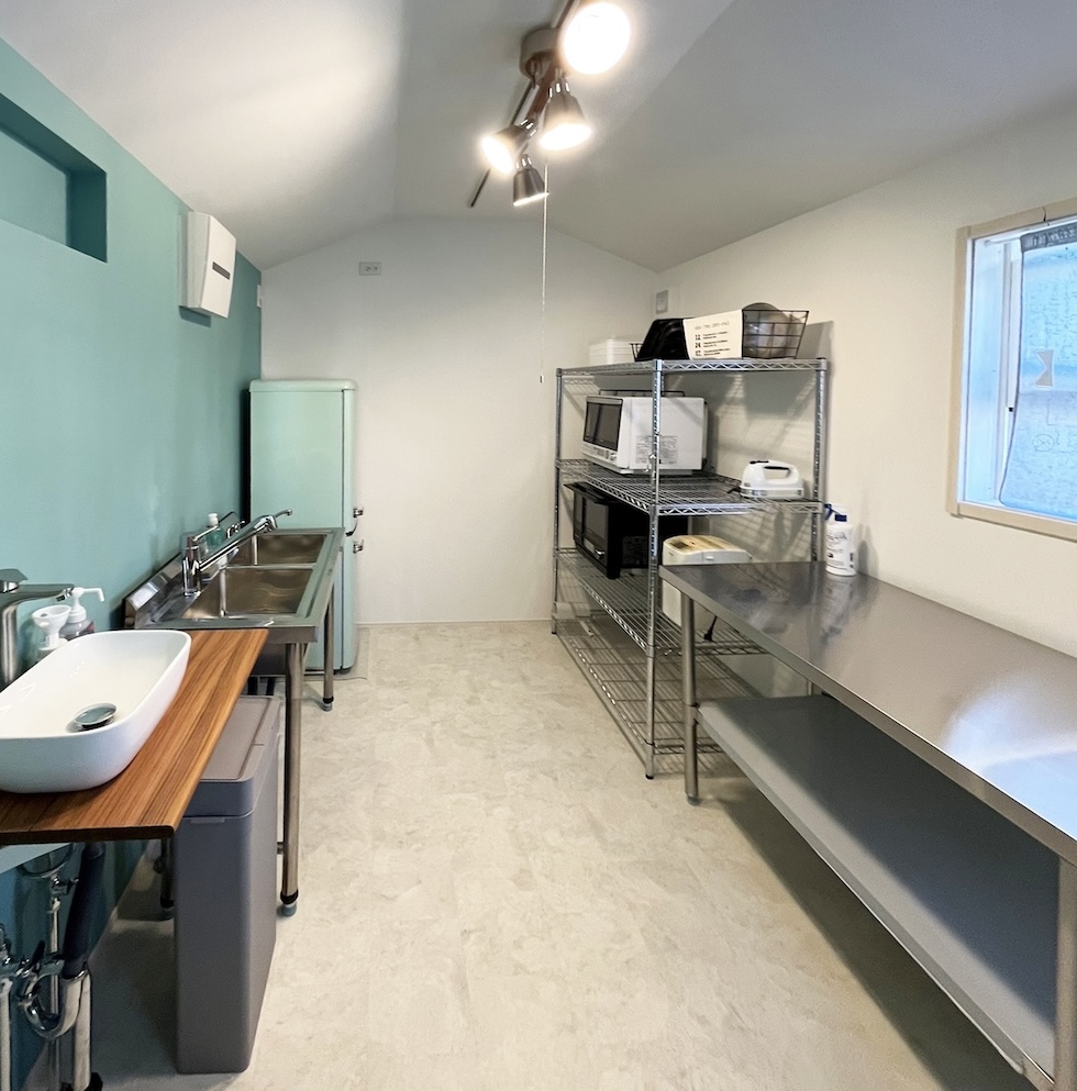 手洗い場、業務用シンク、作業台、オーブン、ラックなどが綺麗にレイアウトされている小屋の中